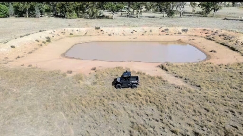 Specialised utility terrain vehicle parked beside a rural farm dam, with open farmland and trees in the background